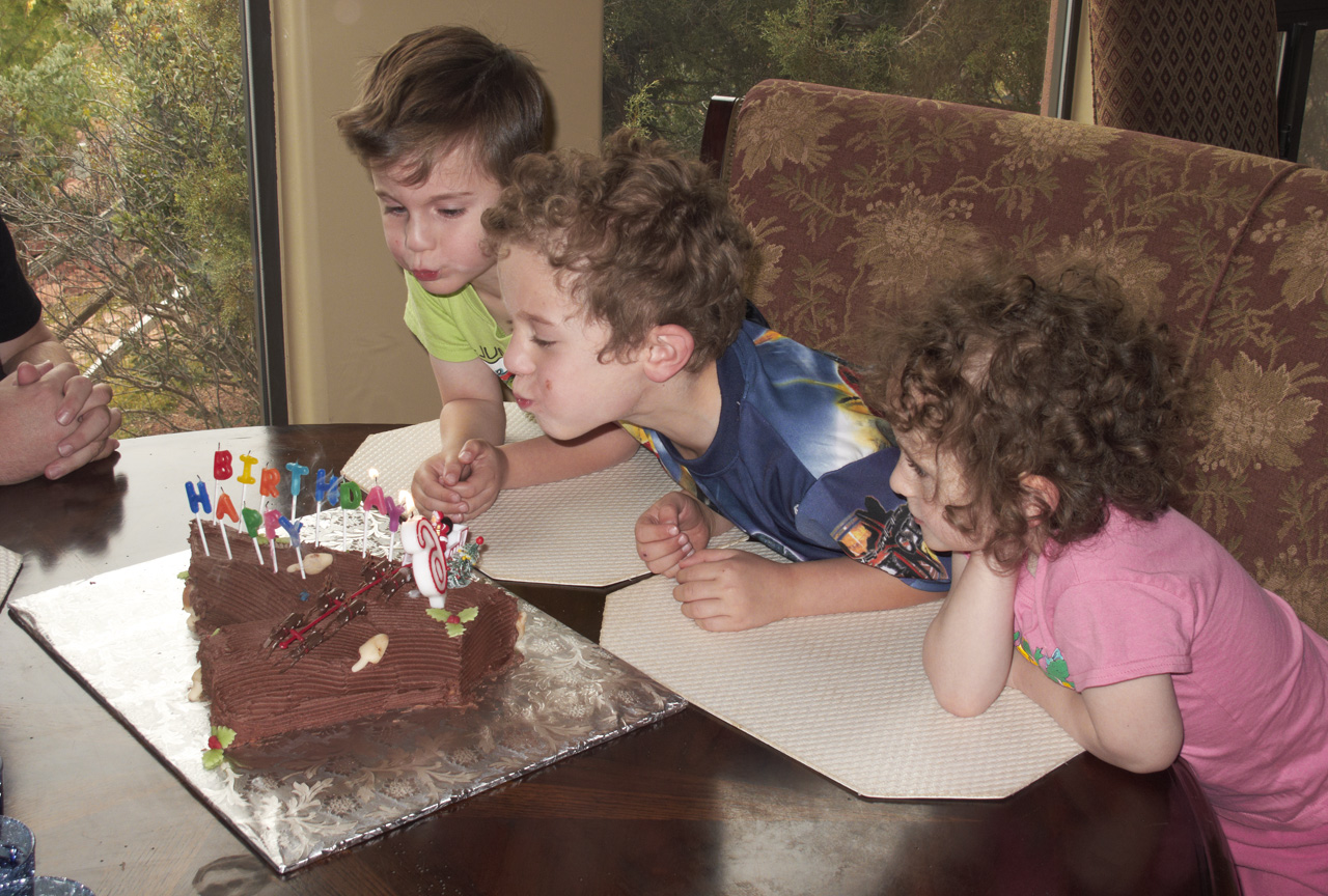 James and John blowing out the candles on their Birthday cake, while Sophia watches