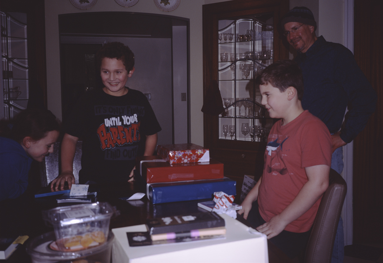 John and James open their Birthday gifts, while Sophia and Marc watch, in the kitchen