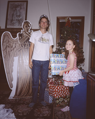 Dan standing before the DOCTOR WHO Weeping Angel cardboard cutout, while Sophia holds a gift in her hands before the Christmas tree, in the piano room on Christmas morning