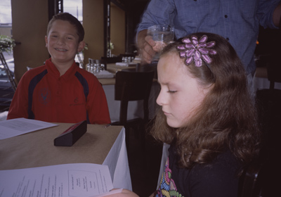 John smiling with his braces showing, while Sophia looks at the menu, inside CLARK LEWIS restaurant