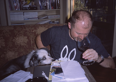 Steve sniffing a glass of red wine, while Marc's new dog Iceman watches attentively, in Marc's den
