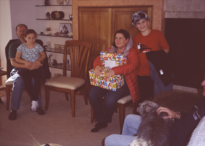 Sophia sitting on Steve's lap, Jackie holding my Birthday gifts, James standing next to Jackie, and Happy sitting on Marc's lap on the sofa in the living room