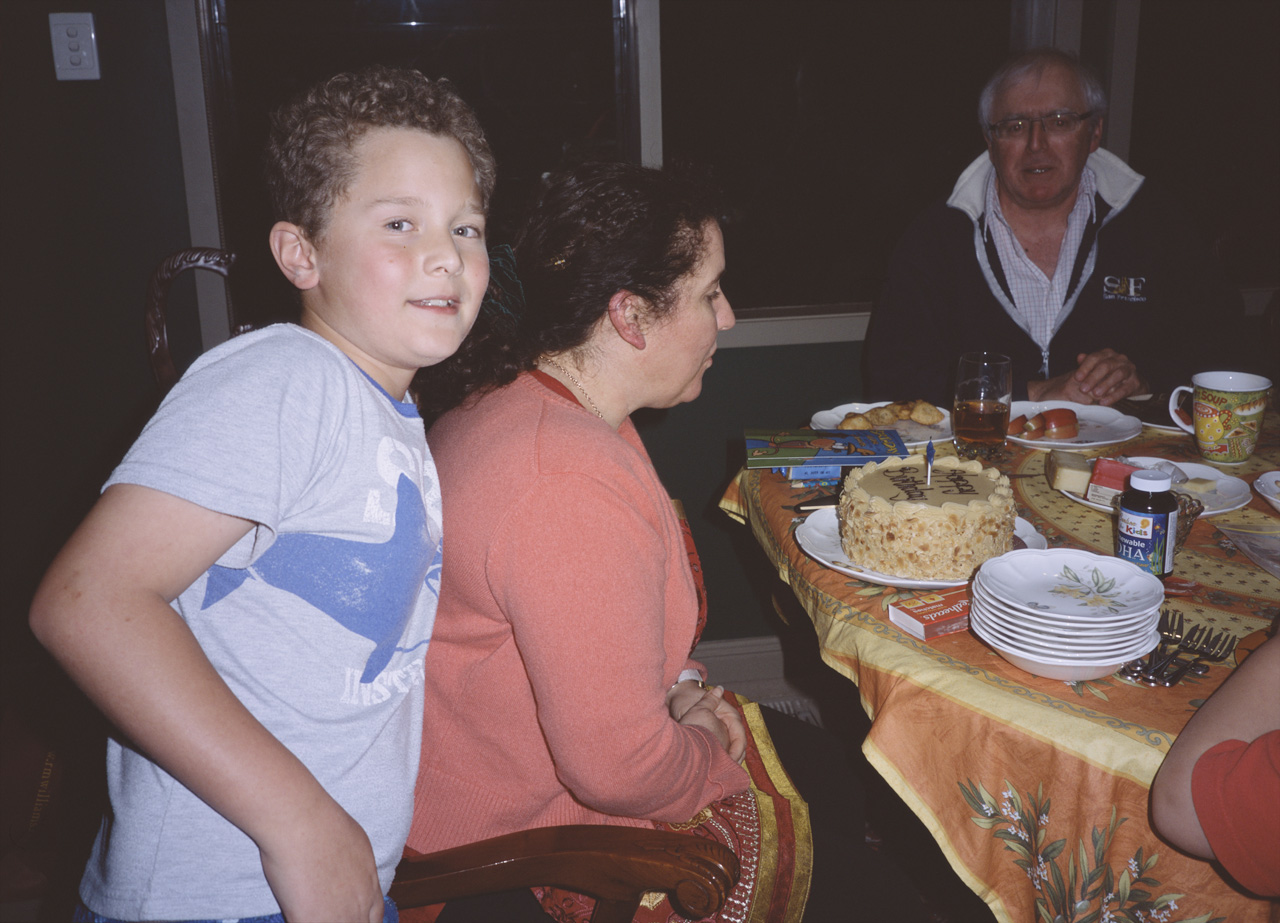John looking at the camera, while Jackie blows out the candles on her Birthday cake, and Stephen watches